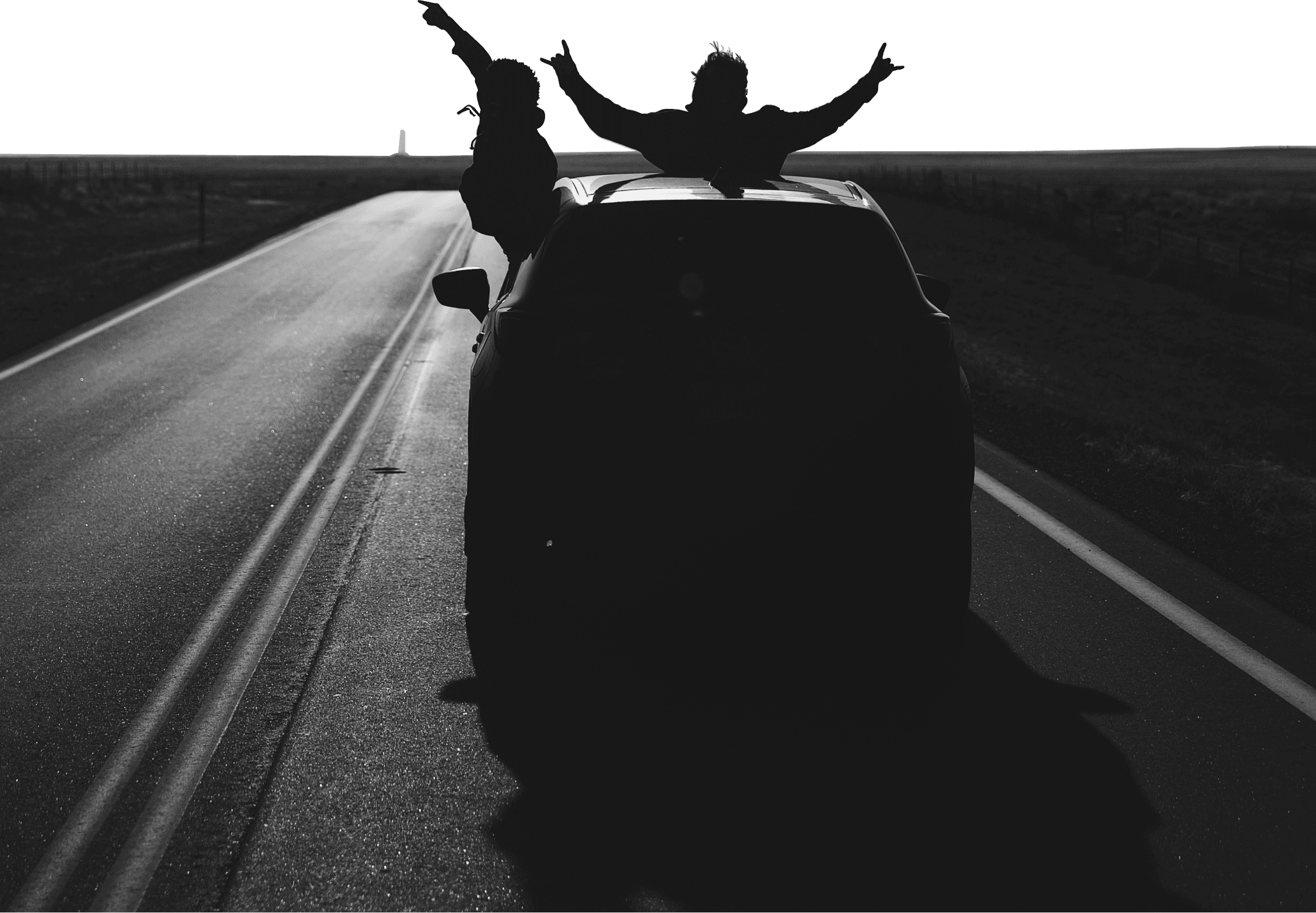 Silhouette of two people joyfully leaning out of a car on an empty road at sunset, arms raised in celebration, capturing a feeling of freedom and adventure.
